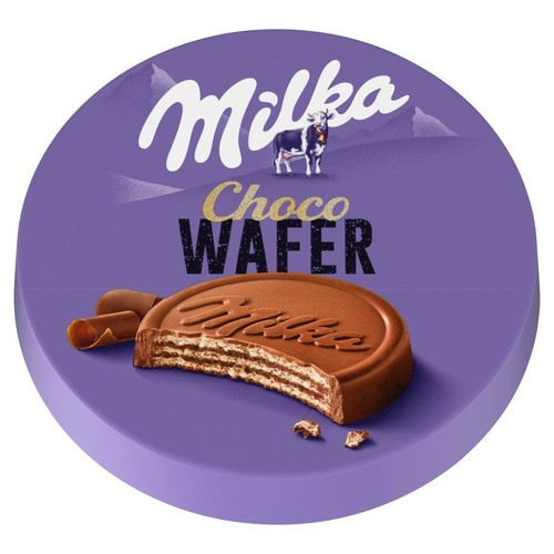 Okrągłe, fioletowe opakowanie produktu Milka Choco Wafer. Na opakowaniu widnieje logo Milka z krową i górami w tle. Centralnie umieszczono grafikę czekoladowego wafelka z widocznym przekrojem warstw i kawałkami czekolady.