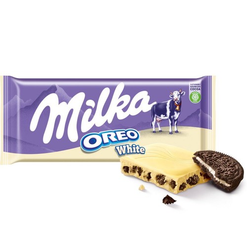 Produkt Milka Oreo White: fioletowo-białe opakowanie czekolady z logo Milka i krową. Na opakowaniu symbol kakao ze zrównoważonych źródeł. Obok opakowania leży kawałek białej czekolady z ciemnymi kawałkami ciastek oraz przekrojone ciastko Oreo.