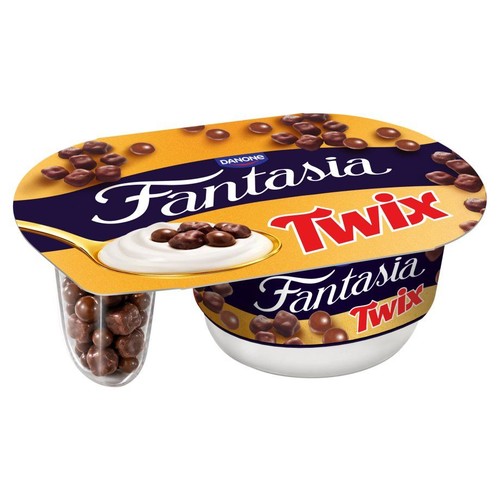 Jogurt Danone Fantasia Twix w białym kubeczku z pomarańczową pokrywką. Obok przezroczysty pojemnik z czekoladowymi kulkami.