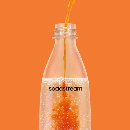 Pomarańczowy koncentrat wlewany do butelki SodaStream z wodą gazowaną. Płyn miesza się, tworząc bąbelki.