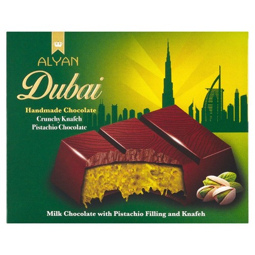 Produkt ALYAN Dubai: ręcznie robiona czekolada mleczna z nadzieniem pistacjowym i Knafeh. Na opakowaniu grafika przedstawiająca przekrojony baton czekoladowy z żółtym wnętrzem oraz orzechy pistacjowe.