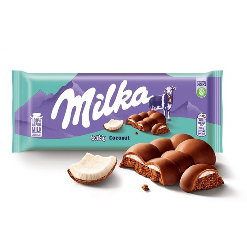 Czekolada Milka Bubbly Coconut w opakowaniu z górskim krajobrazem. Na etykiecie "100% czekolada z alpejskiego mleka". Przed opakowaniem leży świeży kawałek kokosa i rozłamane kostki czekolady, ukazujące puszyste, białe nadzienie kokosowe.