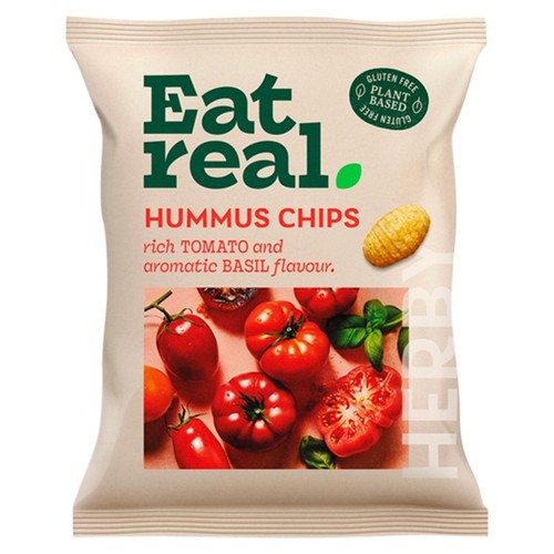 Chipsy hummusowe Eat Real w beżowym opakowaniu. Na etykiecie widnieje nazwa produktu, informacja o smaku pomidorów i aromatycznej bazylii, oraz ikony "bezglutenowe" i "roślinne". Grafika przedstawia pomidory i bazylię.