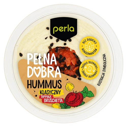 Okrągłe, przezroczyste opakowanie hummusu Perla Klasyczny. Na wierzchu jasnego hummusu widoczny jest czerwony topping Bruschetta z czarnymi nasionami. Etykieta informuje, że produkt jest bez dodatku konserwantów i źródłem błonnika.