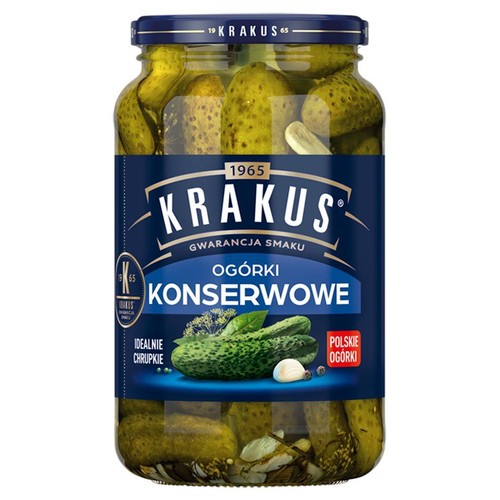 Szklany słoik ogórków konserwowych marki Krakus. Na ciemnoniebieskiej etykiecie napis "Ogórki Konserwowe", "Gwarancja Smaku", "Idealnie Chrupkie" i "Polskie Ogórki". W słoiku widoczne całe ogórki, czosnek i koper.