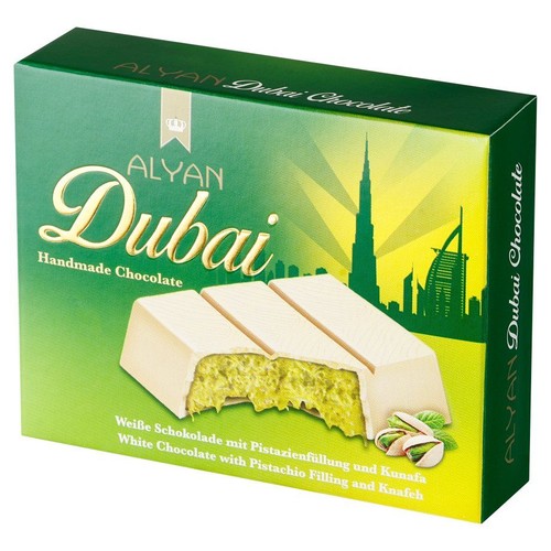 Zielone pudełko czekolady ALYAN Dubai Handmade Chocolate. Na opakowaniu grafika przedstawiająca białą czekoladę z widocznym zielonym nadzieniem pistacjowym i kunafą. W tle złota sylwetka panoramy Dubaju.