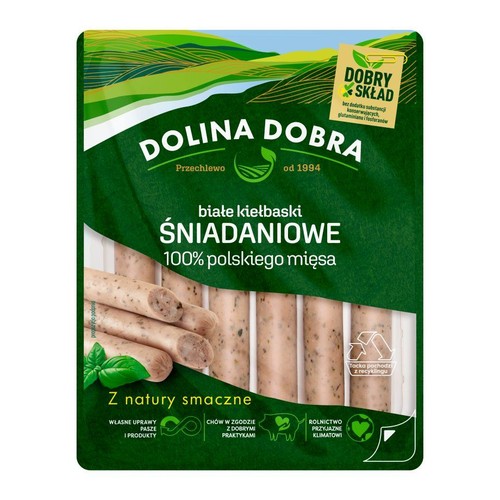Opakowanie białych kiełbasek śniadaniowych Dolina Dobra, 100% polskiego mięsa, z dobrym składem. Widoczne kiełbaski i listki bazylii.