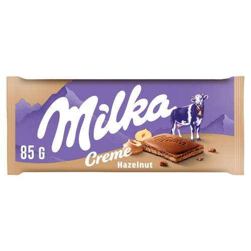 Opakowanie czekolady Milka Creme Hazelnut o wadze 85 g. Fioletowo-beżowe opakowanie z logo Milka, wizerunkiem krowy, górskim krajobrazem oraz kawałkiem czekolady z kremem i orzechami laskowymi.