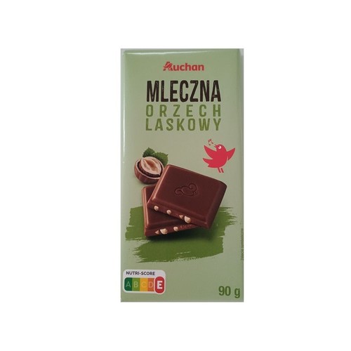 Produkt: czekolada mleczna Auchan z orzechami laskowymi, waga 90 g. Opakowanie w odcieniach zieleni z grafiką orzecha laskowego, dwóch kostek czekolady z kawałkami orzechów oraz śpiewającego czerwonego ptaszka.