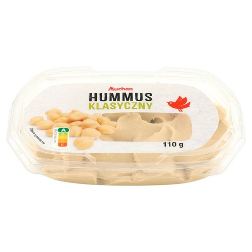 Produkt Auchan Hummus Klasyczny w prostokątnym, przezroczystym pojemniku z tworzywa sztucznego. Etykieta zawiera nazwę "HUMMUS KLASYCZNY", logo Auchan i symboliczną ilustrację ciecierzycy obok hummusu. Waga netto 110 g.
