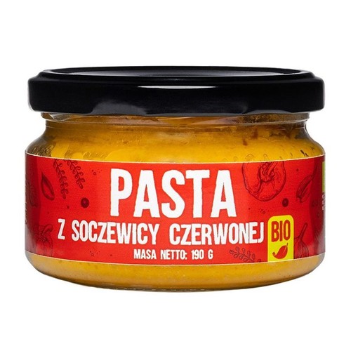Produkt spożywczy: pasta z czerwonej soczewicy BIO, zapakowana w przezroczysty szklany słoik z czarną zakrętką. Czerwona etykieta zawiera biały tekst "PASTA Z SOCZEWICY CZERWONEJ BIO" oraz informację o masie netto 190 g.