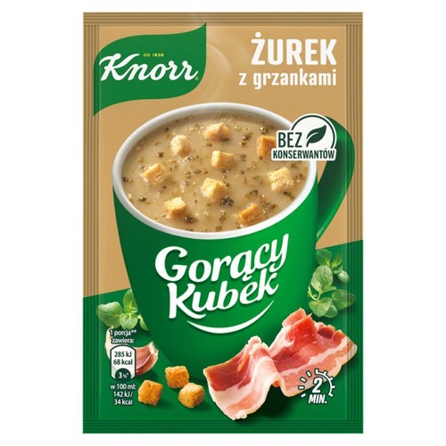 Saszetka Knorr Gorący Kubek Żurek z grzankami. Widoczna grafika zielonego kubka z zupą, na wierzchu chrupiące grzanki. Obok leżą kawałki boczku i świeże zioła. Produkt bez konserwantów. Gotowy w 2 minuty.