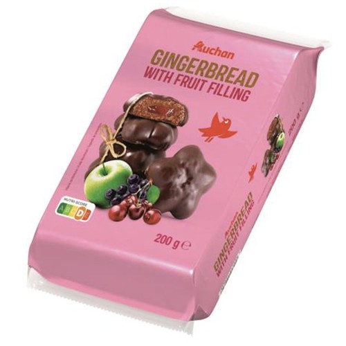 Opakowanie produktu Auchan Pierniki z nadzieniem owocowym, 200 g. Na różowym tle widnieje ilustracja czekoladowych pierników, w tym jeden przekrojony, ukazujący czerwone nadzienie. Obok leżą świeże owoce: jabłko, winogrona i wiśnie.