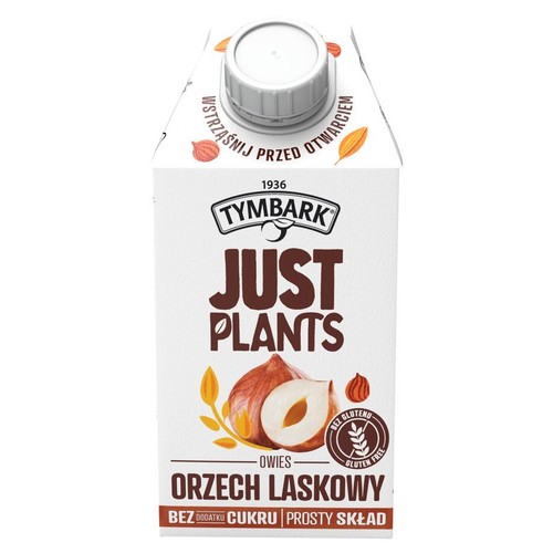 Białe opakowanie Tymbark Just Plants Owies Orzech Laskowy. Produkt bez glutenu i dodatku cukru, z prostym składem. Widoczne orzechy laskowe i liście owsa. Na górze instrukcja "Wstrząśnij przed otwarciem".