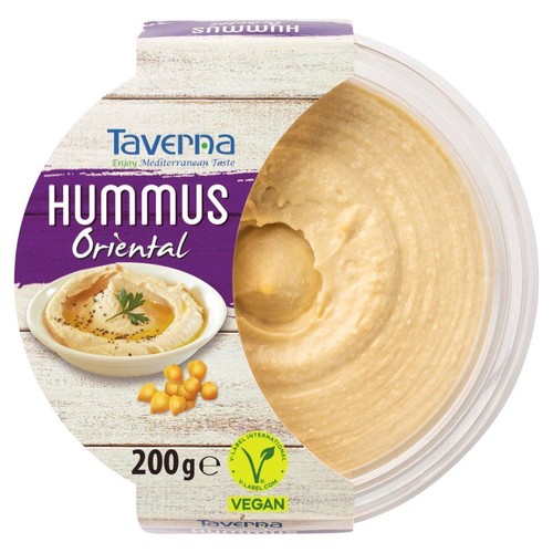 Hummus Oriental marki Taverna, 200g, w przezroczystym, okrągłym pojemniku. Na etykiecie, częściowo zakrywającej produkt, widnieje nazwa "Hummus Oriental" oraz grafika miseczki z hummusem, ciecierzycą i świeżą natką pietruszki. Produkt jest wegański.