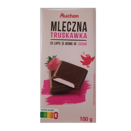 Biało-różowe opakowanie czekolady Auchan Mleczna Truskawka, 100 g. Produkt o smaku mleka i truskawki. Na froncie grafika przedstawiająca przekrojone czekoladki z białym nadzieniem, czerwoną truskawkę i śpiewającego ptaszka.