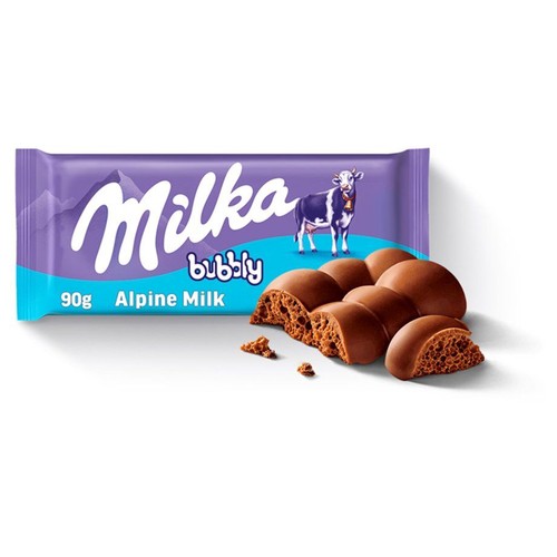 Produkt Milka Bubbly 90g. Fioletowe opakowanie z napisem Milka i krową. Obok opakowania leży kilka kostek czekolady mlecznej, z których część jest przełamana, prezentując charakterystyczną, porowatą teksturę.