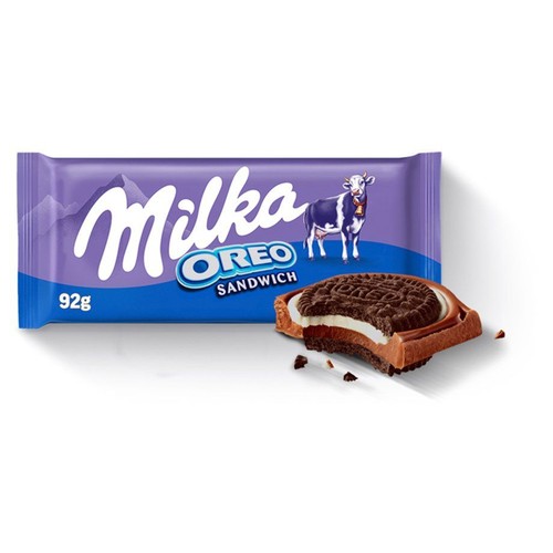 Fioletowe opakowanie czekolady Milka Oreo Sandwich 92g z białym logo Milka, napisem Oreo Sandwich i grafiką krowy. Obok leży przekrojony baton czekoladowy z warstwą białego kremu i ciemnym ciastkiem Oreo.