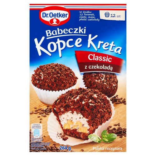 Opakowanie Dr. Oetker Babeczki Kopce Kreta Classic z czekoladą, 264g. Przedstawia trzy babeczki z ciemną posypką, jedna z nich jest przekrojona, ukazując kremowe nadzienie i kawałki banana. Produkt zawiera mieszankę na 12 babeczek.