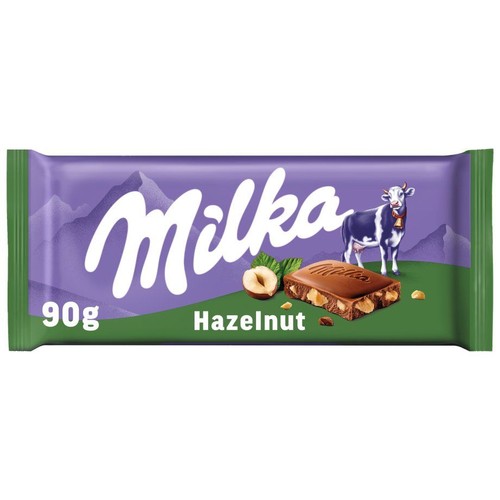 Fioletowe opakowanie czekolady Milka z zielonymi bokami, o wadze 90g. Na opakowaniu widnieje logo Milka, fioletowa krowa oraz grafika gór. Obok napisu "Hazelnut" znajduje się kawałek czekolady z orzechami laskowymi i całe orzechy.