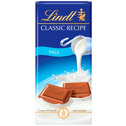 Czekolada Lindt Classic Recipe, mleczna. Opakowanie w kolorze granatowym z elementami błękitu. Na froncie grafika przedstawiająca mleko wylewające się z dzbanka, otoczone rozpryskami, oraz dwie kostki czekolady mlecznej.