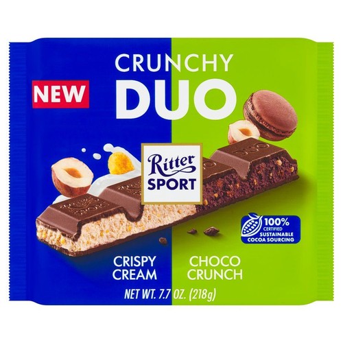 Opakowanie czekolady Ritter Sport Crunchy Duo, 218g. Na niebiesko-zielonym tle widoczny przekrój batonika z dwoma nadzieniami: chrupiącym kremem i choco chrupkami. Obok orzechy laskowe i makaronik. Certyfikowane kakao.