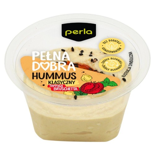 Hummus Perla Pełna Dobra Klasyczny w przezroczystym plastikowym kubku. Na jasnobeżowym hummusie widoczny jest czarny sezam. Etykieta informuje o "Topping Bruschetta" oraz że produkt jest bez dodatku konserwantów i źródłem błonnika.