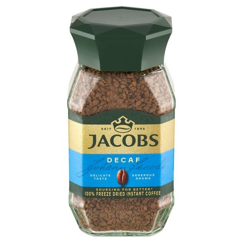 Szklany słoik kawy rozpuszczalnej Jacobs Decaf, 100% liofilizowanej. Ma ciemnozieloną nakrętkę i etykietę w kolorach złotym i niebieskim. Na etykiecie widnieje napis "Delikatny smak" i "Bogaty aromat".