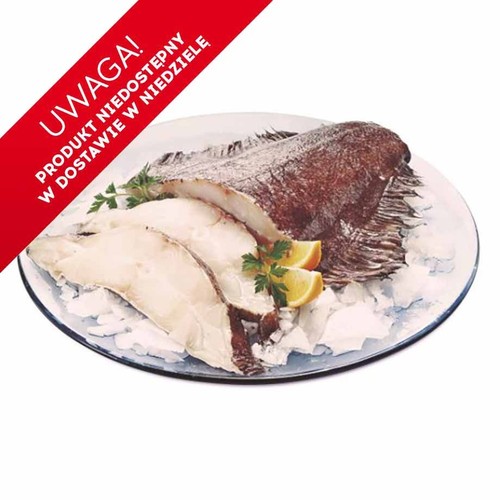 Świeży halibut tusza luz, prezentowany na szklanym talerzu. Widoczna cała ryba o ciemnej skórze oraz kilka białych, grubych filetów. Wszystko ułożone na kruszonym lodzie, ozdobione plasterkami cytryny i świeżą natką pietruszki.