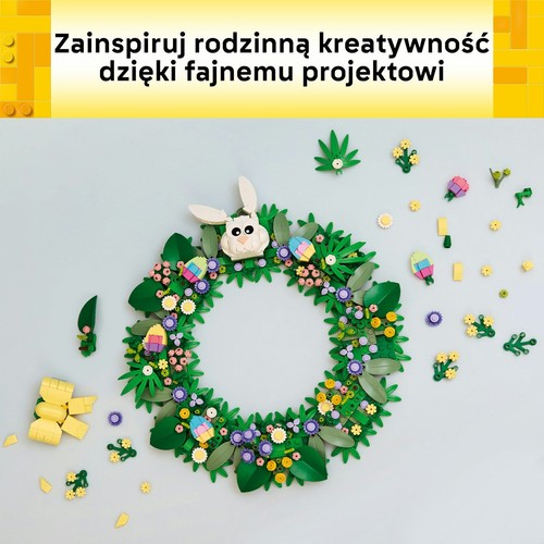 Okrągły wieniec LEGO wykonany z zielonych liści i gałązek, ozdobiony różnobarwnymi kwiatami, kolorowymi pisankami i białą głową królika. Wokół rozłożone są dodatkowe klocki do budowy.