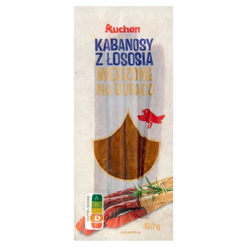 Białe opakowanie Auchan Kabanosy z łososia wędzone na gorąco, 100g. W centralnej części widoczne są brązowe kabanosy. Na dole opakowania znajduje się ilustracja kabanosów z zielonym rozmarynem.