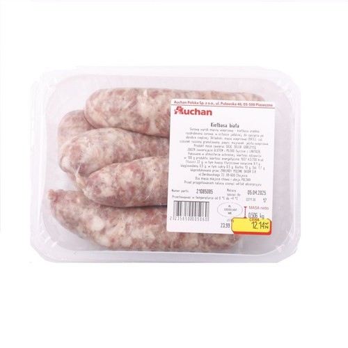 Cztery surowe białe kiełbasy w przezroczystym plastikowym opakowaniu. Produkt marki Auchan, z etykietą zawierającą nazwę "Kiełbasa biała" oraz masę netto 0,506 kg. Kiełbasa ma jasnoróżowy kolor z widocznymi kawałkami mięsa.