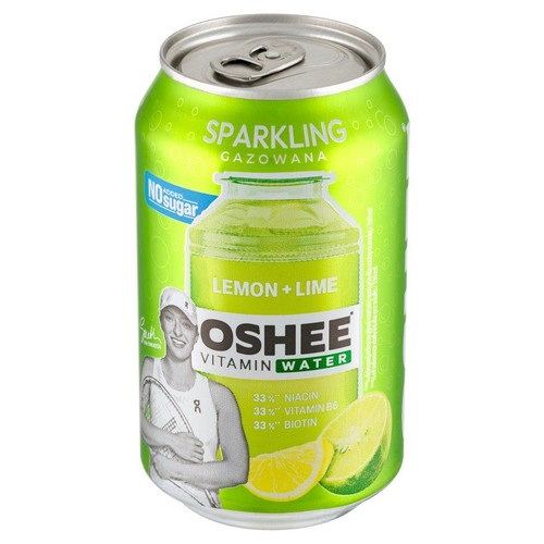 Zielona puszka OSHEE Vitamin Water Lemon + Lime, napój gazowany, bez cukru. Na etykiecie grafika kobiety z rakietą tenisową, symbolizująca sportowca. Widoczne plasterki cytryny i limonki. Zawiera 33% niacyny, witaminy B6 i biotyny.