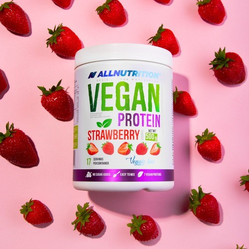 Białe opakowanie ALLNUTRITION Vegan Protein Strawberry 500g. Na etykiecie widnieje napis "Vegan Protein Strawberry", waga 500g, informacja o 17 porcjach, braku cukru, łatwości mieszania i 7 białkach roślinnych. Produkt leży na różowym tle, otoczony świeżymi truskawkami.
