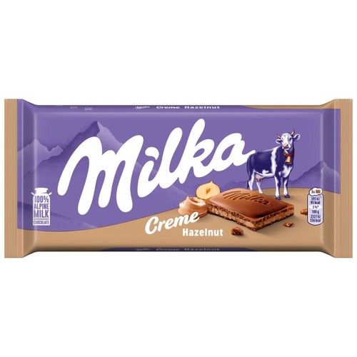 Fioletowe opakowanie czekolady Milka Krem Orzechowy 100g. Na nim białe logo Milka, góry, krowa i kawałek czekolady z kremem orzechowym oraz orzechy laskowe. Zawiera 100% alpejskiego mleka.