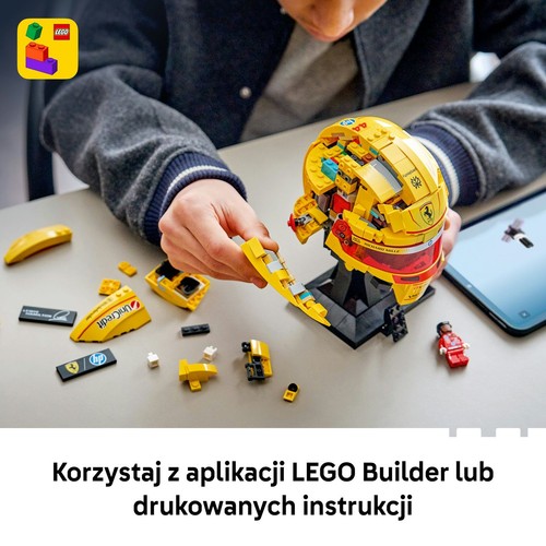 Osoba w szarej bluzie składa żółty kask wyścigowy LEGO Ferrari z czerwonym wizjerem i naklejkami sponsorów. Na stole leżą rozłożone klocki, a obok tablet z otwartą aplikacją LEGO Builder, pokazującą instrukcje.