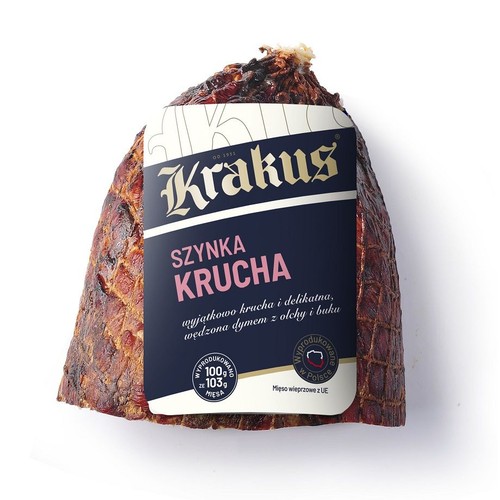 Produkt Krakus Szynka Krucha, kawałek wędzonej szynki wieprzowej. Etykieta informuje o wyjątkowej kruchości i delikatności, wędzeniu dymem z olchy i buku. Wyprodukowano w Polsce. Mięso wieprzowe z UE. Widoczna siatka wędzenia.