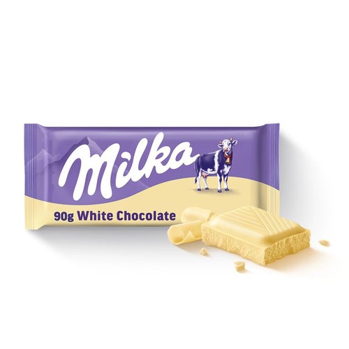 Opakowanie białej czekolady Milka o wadze 90g. Fioletowa etykieta z logo Milka i wizerunkiem krowy na tle gór. Obok opakowania leży odłamany kawałek białej czekolady, ukazujący jej strukturę, oraz kilka mniejszych, zwiniętych wiórków.
