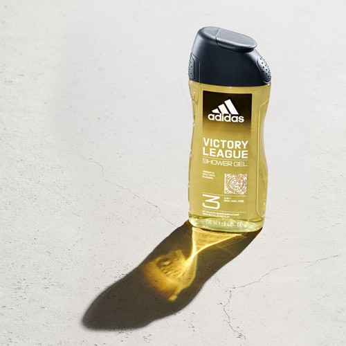 Butelka żelu pod prysznic Adidas Victory League 3 w 1 do ciała, włosów i twarzy, o pojemności 250 ml. Ma przezroczyste opakowanie z czarną nakrętką. Etykieta informuje o zapachu żywym i pikantnym z guaraną. Stoi na jasnej, teksturowanej powierzchni.