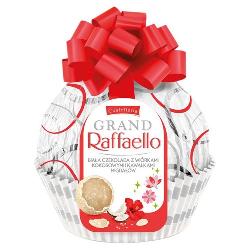 Produkt Grand Raffaello w eleganckim, białym opakowaniu prezentowym z czerwoną kokardą na szczycie. Etykieta przedstawia nazwę produktu oraz opis: biała czekolada z wiórkami kokosowymi i kawałkami migdałów.