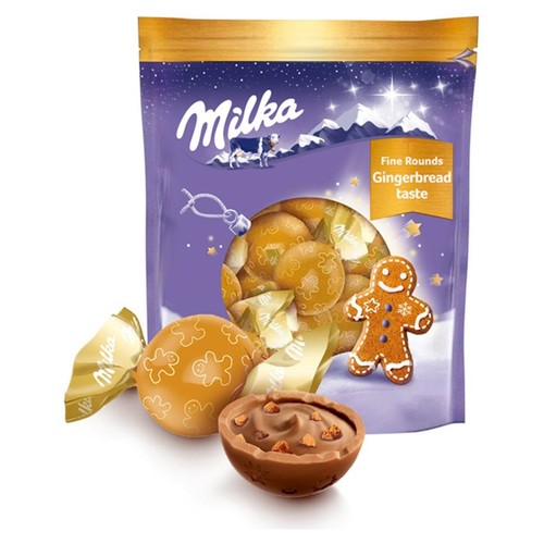 Fioletowa torebka Milka "Fine Rounds Gingerbread taste" z grafiką gór, gwiazd i piernikowego ludzika. Obok leżą trzy okrągłe czekoladki, jedna rozpakowana, jedna częściowo, a jedna przekrojona, ukazująca kremowe nadzienie z kawałkami.