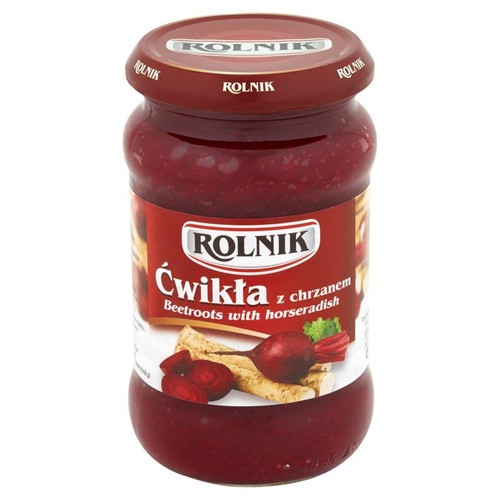 Produkt spożywczy Rolnik: ćwikła z chrzanem w przezroczystym szklanym słoiku. Etykieta jest czerwono-biała, przedstawia buraki i chrzan. Zawartość słoika to ciemnoczerwona masa. Czerwona zakrętka z logo Rolnik.