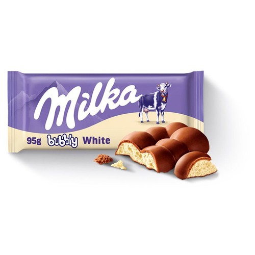 Fioletowe opakowanie czekolady Milka Bubbly White 95g z logo Milka i wizerunkiem krowy. Obok opakowania leży przełamana tabliczka czekolady, ukazująca brązową polewę i białe, napowietrzone, bąbelkowe wnętrze. Widoczne są też drobne okruszki.