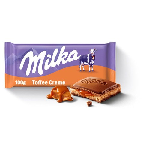 Produkt Milka Toffee Creme 100g. Fioletowe opakowanie z logo Milka, krową i górami. Na opakowaniu napis "Toffee Creme". Obok opakowania leży kawałek czekolady z wytłoczonym logo Milka, rozłamany, ukazujący kremowe nadzienie toffee i karmel.