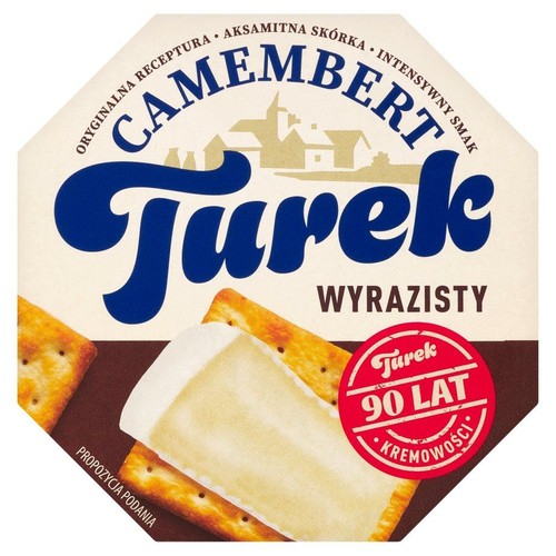 Ośmiokątne opakowanie sera Camembert Turek Wyrazisty. Na kremowym tle duży napis "Turek" i "Camembert". W tle grafika stylizowanego zamku. Na dole propozycja podania: ser na dwóch krakersach.