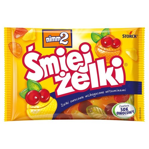 Żółte opakowanie żelków nimm2 Śmiejżelki. Na opakowaniu duży czerwony napis "Śmiejżelki". Widoczne przezroczyste owocowe żelki w kształcie wiśni, pomarańczy, cytryny i liści, niektóre z nich mają uśmiechnięte buźki.
