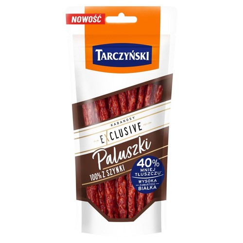 Produkt Tarczyński Kabanosy Exclusive Paluszki w stojącym opakowaniu. Na etykiecie informacja "Nowość", "100% z szynki", "40% mniej tłuszczu" oraz "Wysoka zawartość białka". Przezroczyste okienko ukazuje czerwone kabanosy.