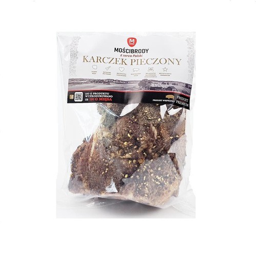 Mościbrody Karczek Pieczony, produkt wieprzowy premium z serca Polski. Mięso w przezroczystym opakowaniu, z widocznymi przyprawami na ciemnobrązowej powierzchni. 100g produktu wyprodukowano ze 100g mięsa.