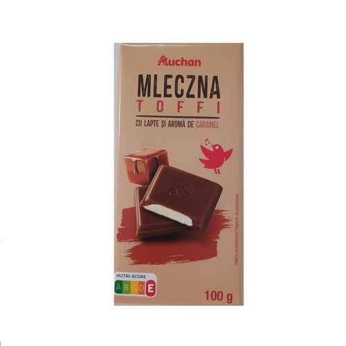 Beżowe opakowanie batonika Auchan Mleczna Toffi z mlekiem i aromatem karmelowym, 100 g. Na froncie grafika dwóch czekoladek, jedna z widocznym białym nadzieniem, oraz kostki karmelu. Obok mały czerwony ptaszek.