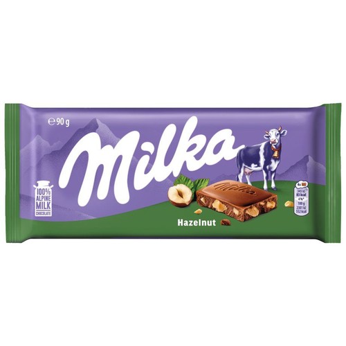 Czekolada mleczna Milka z orzechami laskowymi, waga 90 gramów. Opakowanie jest fioletowe z zielonym paskiem na dole. Zawiera grafikę krowy, górskiego krajobrazu oraz przekrojonego kawałka czekolady z orzechami laskowymi.